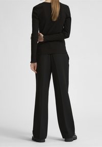 Top negro de manga larga con relieve, escote redondo y dobladillo ligeramente deshilachado, combinado con pantalones negros de pierna ancha y calzado negro grueso.
