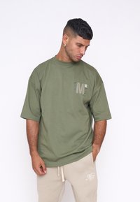 Camiseta de algodón verde con corte relajado, cuello redondo y mangas cortas. Presenta un pequeño gráfico en el lado izquierdo del pecho.