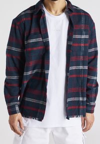 Marinblå och röd rutiga flanellskjorta med knappdesign, med en ficka och fransad nederkant, lager på en vit T-shirt med rund hals.