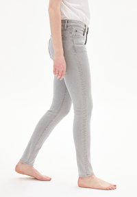 Jeans ajustados de color gris claro con una cintura de altura media, cinco bolsillos y un ligero desgaste. Elaborados en denim con una textura suave.
