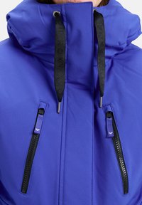 Lila isolierte Jacke mit hohem Kragen, schwarzen Reißverschlüssen, kurzen Ärmeln und Zugband-Akzenten. Verfügt über gebrandete Zugbänder und Seitentaschen.