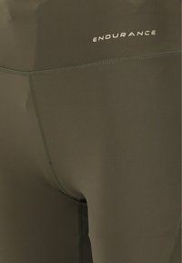 Olijfgroene sportleggings met een gladde stof, platte naden en een klein wit "ENDURANCE" logo op de tailleband.
