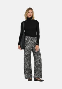Maglione a collo alto nero abbinato a pantaloni grigi a gamba larga con stampa leopardata nera. Modella che tiene una borsa a spalla nera e indossa scarpe flat.