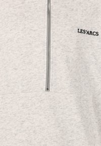 Hellgraues Sweatshirt mit Reißverschlusskragen, aus strukturiertem Material mit schwarzem, gesticktem "LES'ARCS"-Logo auf der Brust.