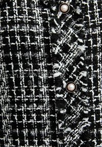Zwart-wit tweedstof met een textuurpatroon en zichtbare draden; bevat een ronde parelknop met decoratieve rand.