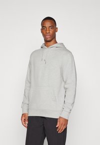Gray hoodie with a drawstring hood, front pocket, and subtle logo on the chest. Soft material and relaxed fit. Paired with black pants.