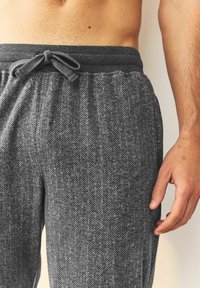 Grau gestreifte Lounge-Hosen im Fischgrätmuster mit elastischem Bund und Kordelzug. Aus weichem Stoff gefertigt, mit subtiler Textur und lockerem Schnitt.
