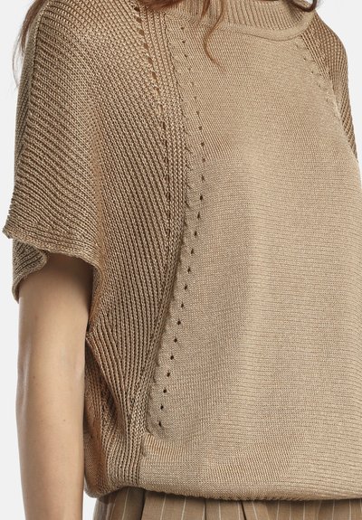 Haut en tricot beige à manches courtes avec textures côtelées et lisses, doté d'un col montant et de petits œillets décoratifs le long du panneau avant.