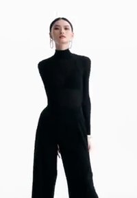 Svart tettsittende jumpsuit med høy hals og lange ermer. Glatt tekstur, bredbent design, og store hoop-øreringer som fremtredende aksenter.