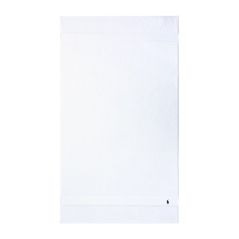 Λευκή βαμβακερή πετσέτα μπάνιου με υφή μπάνιου βρόγχου. Έχει απλό σχέδιο με οριζόντια λωρίδα και μικρό λογότυπο στη γωνία.