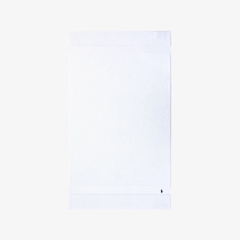Λευκή βαμβακερή πετσέτα μπάνιου με υφή μπάνιου βρόγχου. Έχει απλό σχέδιο με οριζόντια λωρίδα και μικρό λογότυπο στη γωνία.