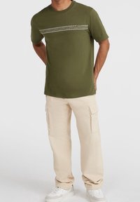 Olijfgroene katoenen t-shirt met een geometrisch patroon op de borst, gecombineerd met beige cargobroeken en witte sneakers.