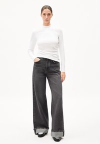 Witte geribbelde lange mouwen top gecombineerd met hoge taille wijde zwarte jeans, met een opgerolde mouw en zijzakken.