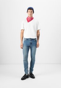 Blue beanie, red bandana, white T-shirt, and distressed light blue skinny jeans. Black shoes complete the outfit on a plain background.