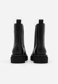 Mustat nahkasaappaat nilkkapituudella, joissa on joustavat sivupaneelit ja takana vetonauhat. Ominaisuuksiin kuuluu paksu musta kumipohja ja sileä pinta.