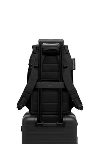 Sac à dos noir avec des bretelles rembourrées et une texture en maille, monté sur une valise rigide noire avec une poignée télescopique.