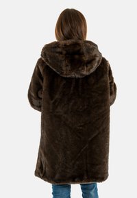 Cappotto di pelliccia marrone con cappuccio, caratterizzato da una consistenza morbida e pelosa. Il design è ampia, con maniche lunghe e una lunghezza al di sotto dei fianchi.