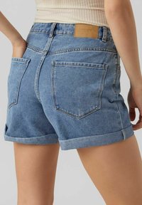 Vaaleansiniset denimshortsit, joissa korkea vyötärö, käännetyt lahkeet ja nahkainen merkkilappu takana. Kaksi takataskua näkyvissä.