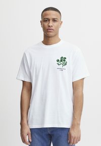 Camiseta de algodón blanca con un estampado floral verde en la parte izquierda del pecho, con mangas cortas y un corte relajado.