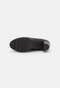Semelle de chaussure en cuir noir avec un motif texturé, présentant un léger talon et un design de semelle pour l'adhérence. Logo circulaire embossé près du talon.