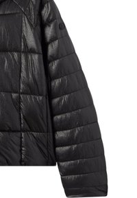 Giacca imbottita nera con finitura lucida, caratterizzata da trame trapuntate e pannelli cuciti. Manica arrotondata con dettagli del logo.