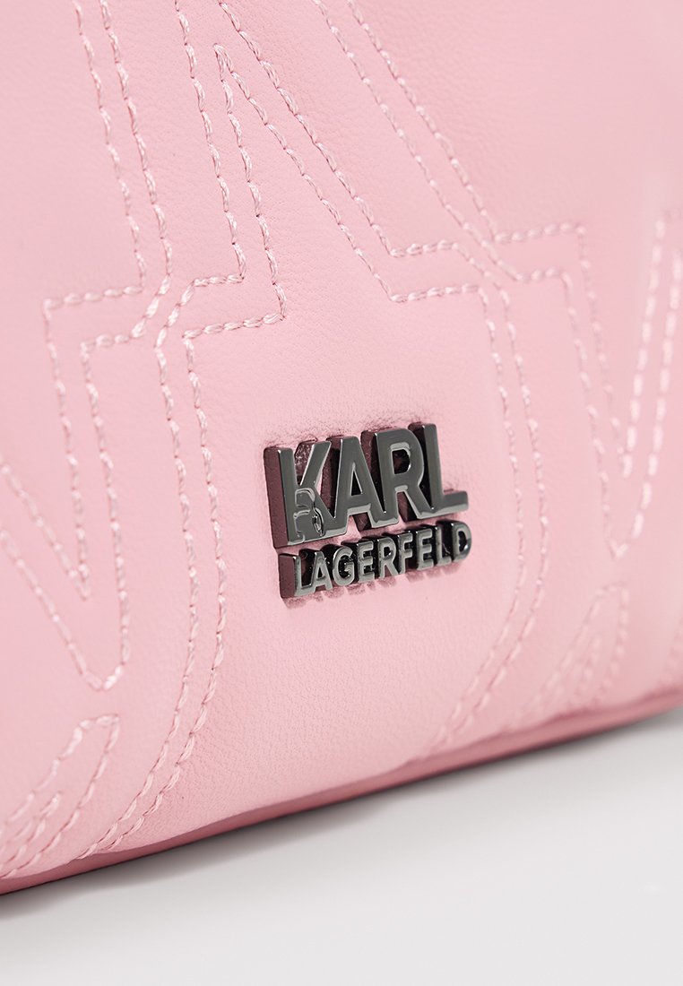 Sac à main en cuir rose avec des coutures gaufrées et un logo de marque métallique. Texture lisse avec une forme rectangulaire et des détails de design subtils.