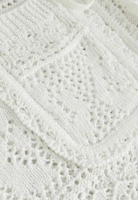 Tissu tricoté blanc présentant un motif géométrique de triangles et de lignes avec des points en relief texturés.