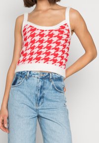 Červený a bílý pletený crop top s motivem psa zubatého se širokými ramínky a chlupatou texturou, kombinovaný s vysokým pasem světlých modrých džín.