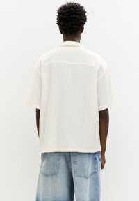 Short-sleeve, textured white shirt with a relaxed fit and collar, paired with loose-fitting blue denim shorts featuring two back pockets.