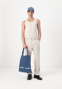 Tan tank top, light beige pants, dark shoes. Holding a blue denim tote bag with white "SAMSOE" logo. Simple, casual outfit.