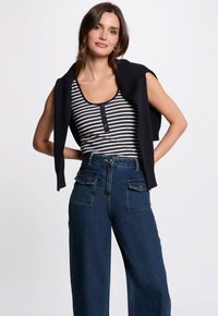 Marineblå cropped sweater lagd ovenpå en sort-hvid stribet tank top med knapper. Højtaljede denim jeans med brede ben og forlommer.