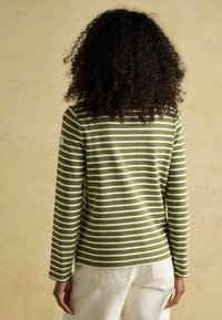 Langärmeliges Oberteil mit grünen und weißen Streifen, Rundhalsausschnitt und Seitenschlitzen, kombiniert mit hellfarbenen Hosen. Die Textur wirkt weich.