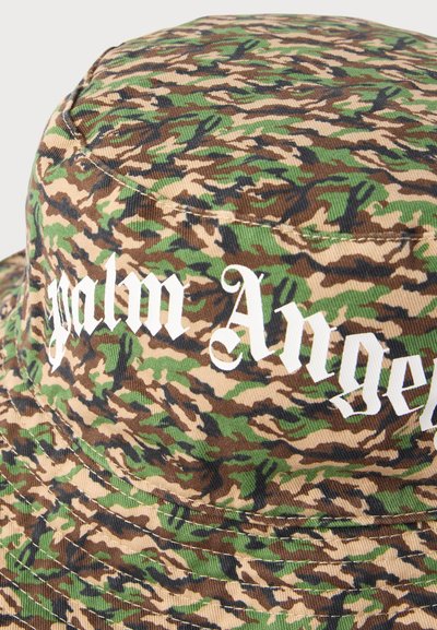 Καπέλο τύπου bucket με καμουφλάζ, αποχρώσεις πράσινου, καφέ και μαύρου, με λευκό κείμενο σε στυλ παλαιάς αγγλικής γραφής που γράφει "palm Angels".