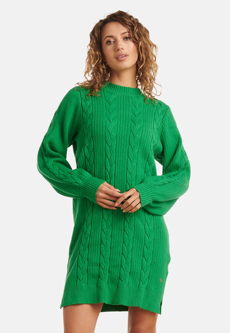 Vestito maglione verde a trecce con maniche lunghe, collo alto, orlo a coste e spacchi laterali per facilitare i movimenti.