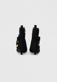 Black suede ankle boots with a small heel, featuring double straps and gold-tone hardware accents on the side and back.