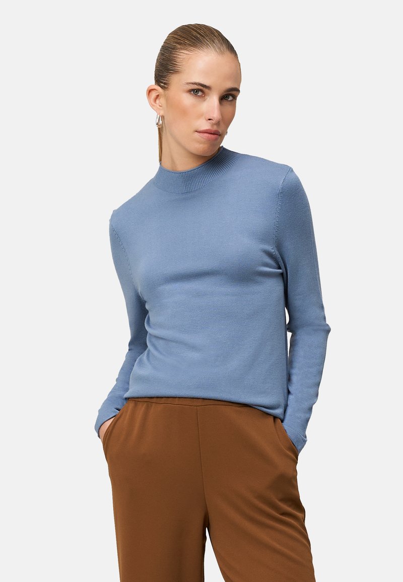 Light blue knit sweater with long sleeves and a high neck, paired with brown trousers. The fabric appears soft with a smooth texture.