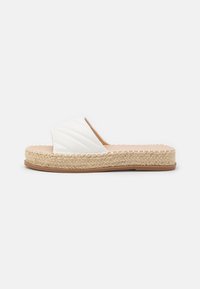 Espadrille blanche à enfiler avec dessus matelassé, semelle intermédiaire en jute tissé et semelle extérieure en caoutchouc. Présente un design à orteils ouverts et plats.