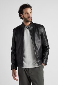 Zwarte leren jas met een slank ontwerp, hoge kraag en ritsluiting. Kenmerkt zich door een soepele textuur en subtiele stikseldetails.