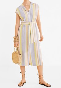 Abito midi a righe in colori pastello con cintura. Presenta maniche corte, bottoni e uno spacco frontale. Borsa in paglia intrecciata e sandali flat.