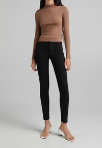 Braun gestreifter Langarm-Top kombiniert mit schwarzen figurbetonten Hosen und klaren Absatzsandalen. Das Outfit zeichnet sich durch ein elegantes, schlankes Design aus.