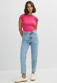 Camisa ajustada de manga corta en color rosa combinada con jeans de tiro alto en azul claro y zapatillas blancas. Diseño sencillo, tejido de algodón, estilo casual.