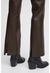 Pantalons en cuir marron avec des fentes sur les côtés au bas, associés à des bottines noires à talon haut avec un talon épais et un bout rond.