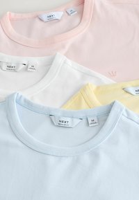 Quatre t-shirts en coton de couleur pastel en rose, blanc, jaune et bleu clair, avec des encolures rondes et des étiquettes de marque "NEXT" visibles.