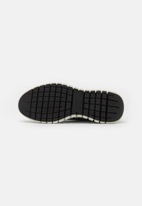 Black rubber shoe sole with a textured, patterned surface and white edging. Includes deep grooves for traction and stabilization.