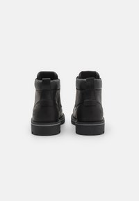 Botas de tobillo de cuero negro con un acabado suave, punta redondeada y forro textil. Con un tirador en la parte posterior y una suela de goma estriada.