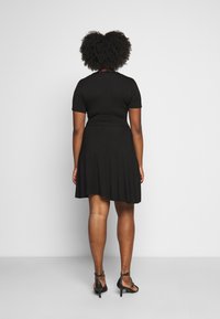 Robe noire à manches courtes avec un corsage ajusté et une jupe évasée. Tissu lisse, longueur genoux, associée à des sandales à talons hauts noires.