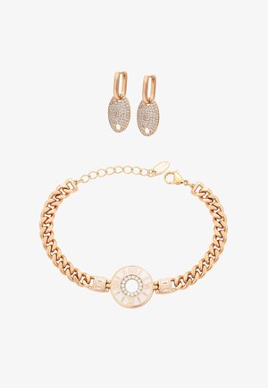 Bransoletka w kolorze złota z rzymskimi cyframi i kryształowymi akcentami, zestawiona ze złotymi kolczykami kołami z owalnymi zawieszkami wysadzanymi kryształami.