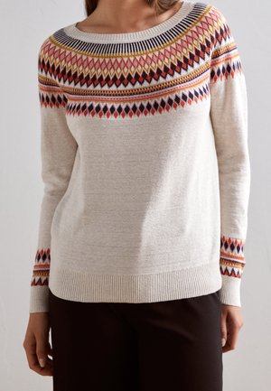 Pull crème avec motif losange multicolore sur le yoke et les poignets, porté avec un pantalon foncé.