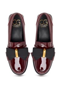 Mocassins en cuir verni bordeaux ornés d'un grand nœud noir et d'un détail de quincaillerie dorée sur une semelle intérieure noire lisse.