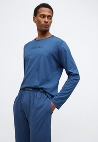 Langærmet blå skjorte med rund halsudskæring og broderet logo; matchende blå bukser med elastisk talje og mærke detaljer.